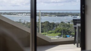 Een balkon met uitzicht op water, groen en een verre brug.