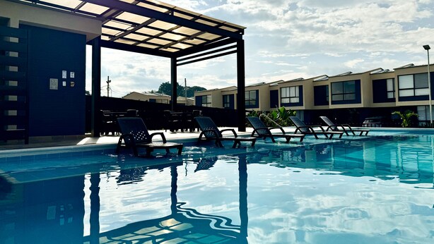 Una piscina con sillones de descanso y una zona de estar cubierta.