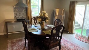 Un coin repas comprenant une table en bois, des chaises, un vase avec des fleurs, une cuisinière encastrée et un réfrigérateur.