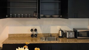 Une cuisine avec des meubles de couleur noire, un plan de travail en granit, un évier, un grille-pain, une bouilloire et un four à micro-ondes.