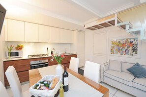 Une cuisine moderne avec des meubles blancs, une table à manger agrémentée d’une bouteille de vin et un canapé blanc dans l’espace salon.