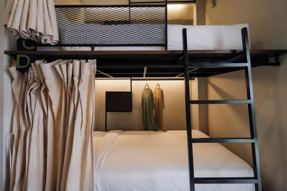 A bunk bed room with a ladder, a hanging rack, and a wall-mounted TV.