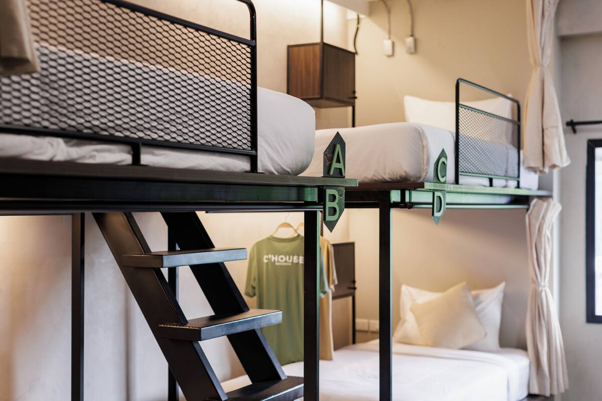 A bunk bed with a mesh headboard, a green T-shirt hanging on the wall, and a bedside table with a lamp.