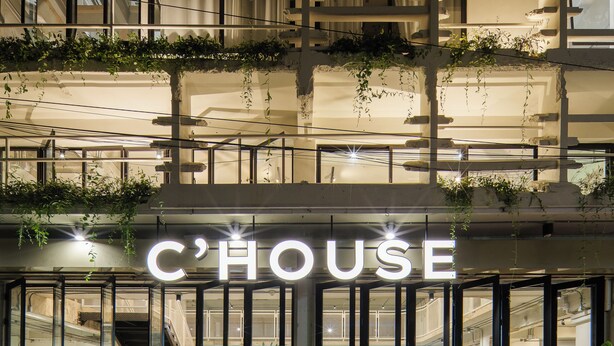 Un bâtiment sur lequel on peut lire l’inscription « C’HOUSE » et qui possède de nombreux balcons ornés de plantes.