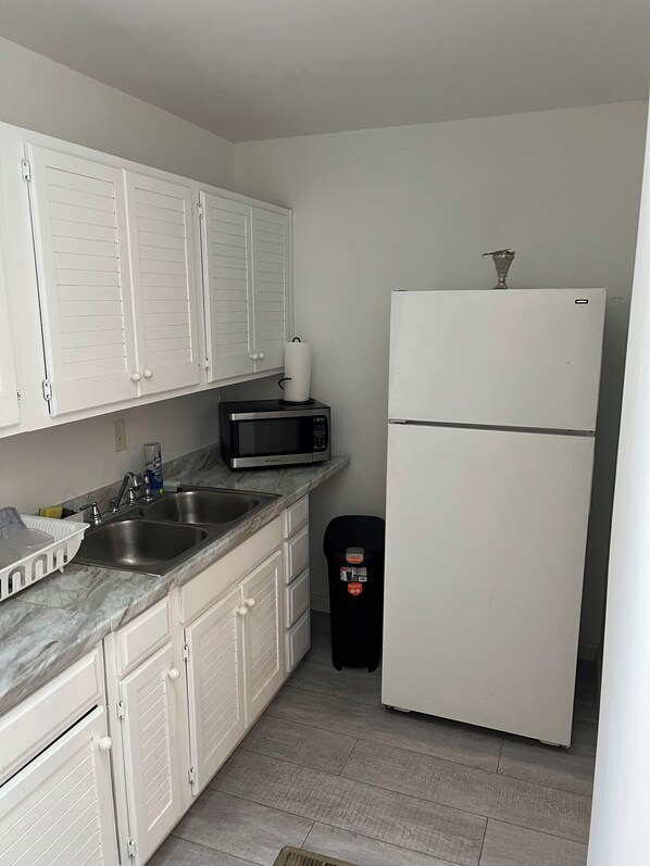 A compact kitchen with white cabinets, a stainless steel sink, a microwave, and a white refrigerator. - Cozy private suite, amenities. 5 min Saint Francis Hospital, Woodland Hills mall (Tulsa)