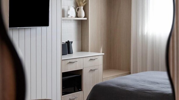 A modern bedroom with a bed, a TV mounted on the wall, a ceiling fan, and a built-in wardrobe.