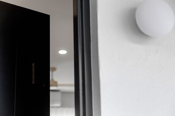 A modern interior with a black door marked with the number 1, a white wall, and a spherical light fixture.