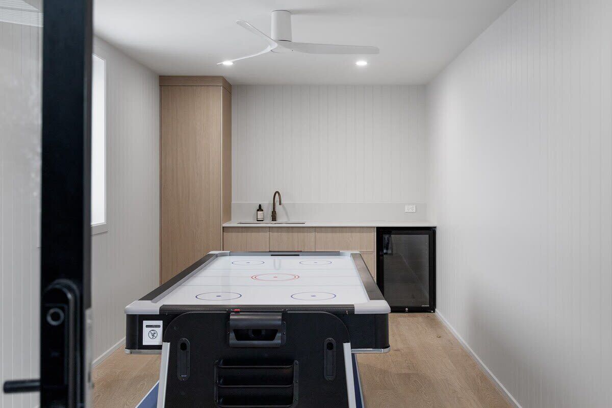 Habitación con mesa de billar, ventilador de techo, kitchenette pequeña y puerta que da a otra habitación.