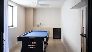 A pool table in a room with a window, a ceiling fan, and a kitchen area. - The Lodge - Room 2 - Luxury Central private Rooms, Free wifi (Mount Gambier)