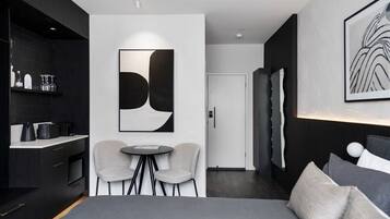 Moderni hotellihuone, jossa on suuri sänky, pieni ruokailutila kahdella tuolilla, keittiö sekä suuri abstrakti maalaus seinällä.