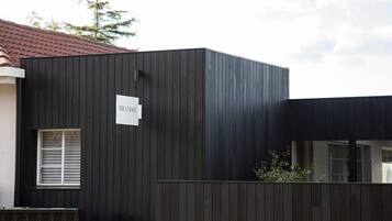 A modern building with a dark facade, a small window with blinds, and a sign with text.