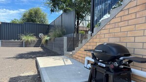 Una parrilla Weber apoyada contra una pared de ladrillo, con un escalón de hormigón que lleva a una escalera.