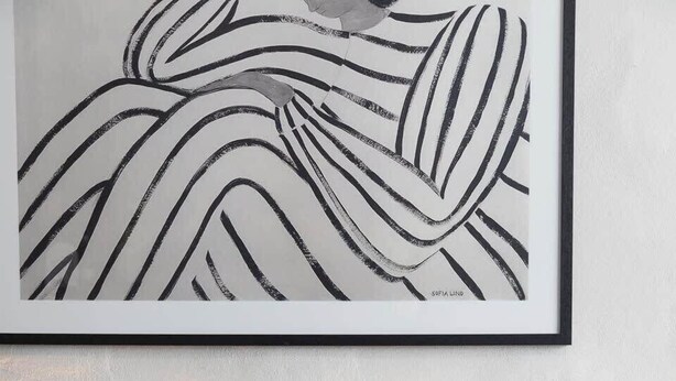 Un dormitorio moderno con cabecera gris, una mesita de noche redonda blanca y una obra de arte abstracto enmarcada.