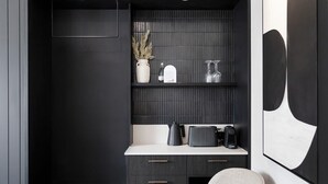 Una habitación moderna con una decoración oscura, una encimera blanca, una cafetera negra y un jarrón con plantas secas.