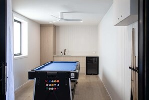 Ein Billardtisch in einem Raum mit Fenster, Deckenventilator und Küchenbereich.