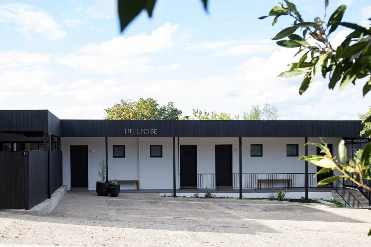 A modern building named "The Lodge" with a minimalist design, featuring a flat roof, a central entrance, and a small outdoor seating area.