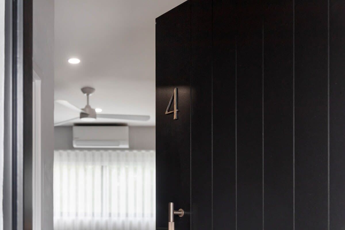 Un intérieur moderne avec une porte sombre portant le numéro 4, un ventilateur de plafond et un radiateur.