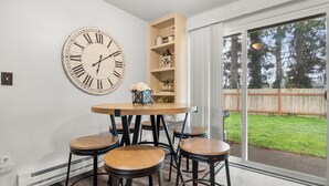 A dining area with a round table, four stools, a large wall clock, and a wooden bookshelf. - Cozy 3BR modern farmhouse in Rochester with stone fireplace, fenced yard, and easy I-5 access. (Rochester)