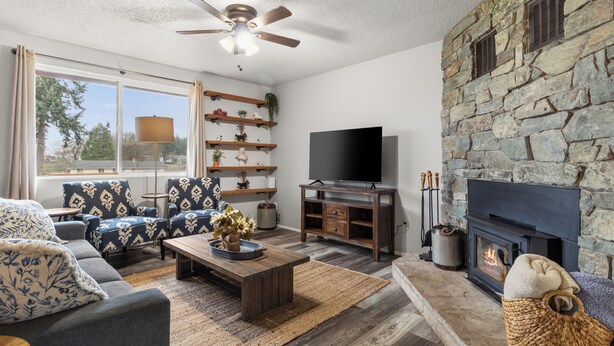 A living room with a stone fireplace, a flat-screen TV, and a ceiling fan. - Cozy 3BR modern farmhouse in Rochester with stone fireplace, fenced yard, and easy I-5 access. (Rochester)