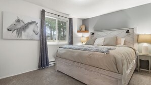 A bedroom with a large bed, a headboard, two bedside lamps, a wall-mounted shelf with a decorative item, and a window with curtains. - Cozy 3BR modern farmhouse in Rochester with stone fireplace, fenced yard, and easy I-5 access. (Rochester)