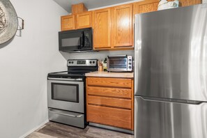 A kitchen with wooden cabinets, a stainless steel refrigerator, a microwave, a stove, and a toaster.