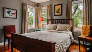 Ein Schlafzimmer mit einem hölzernen Bett, einem Nachttisch, einem Stuhl und einem Fenster mit Vorhängen.