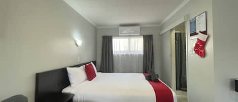 A hotel room with a bed, a desk, a chair, a TV, and a window with curtains.