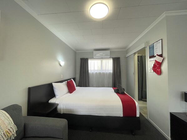 Habitación de hotel con cama, escritorio, silla, televisor y ventana con cortinas.