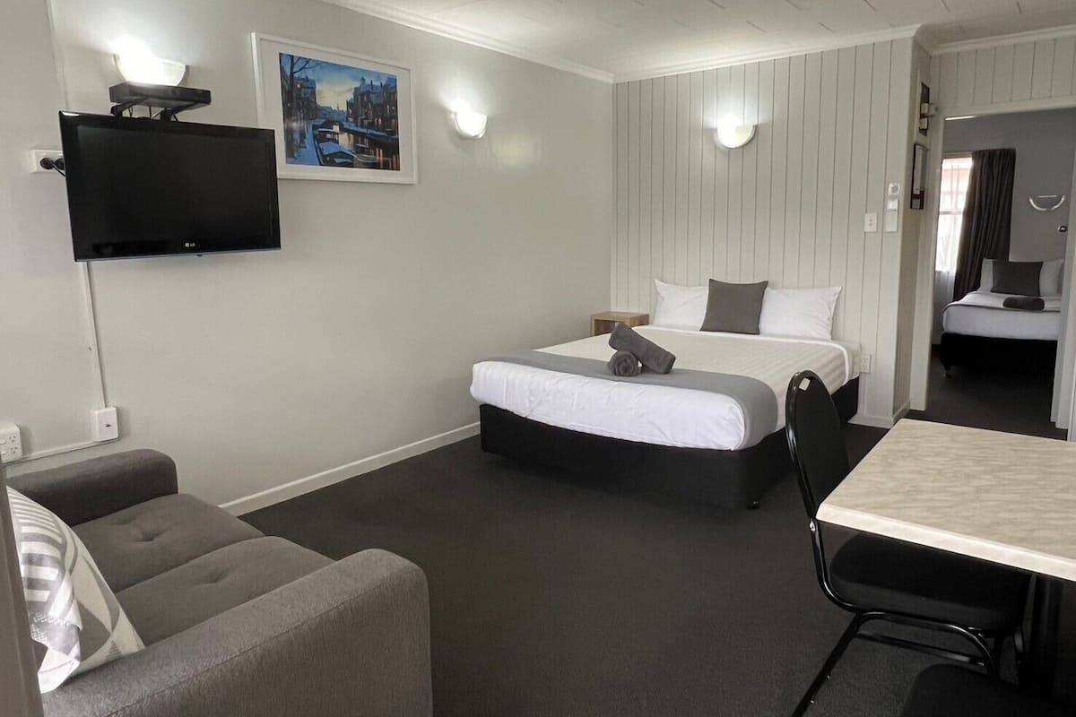 Una habitación de hotel con cama, escritorio, silla, televisor y un cuadro en la pared.
