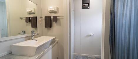 Un baño moderno con un espejo grande, un lavabo blanco y una zona de ducha.