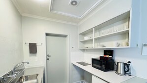 A compact kitchenette with a stainless steel sink, a microwave, a kettle, and a small refrigerator. - Kensington Motel (Whangarei)