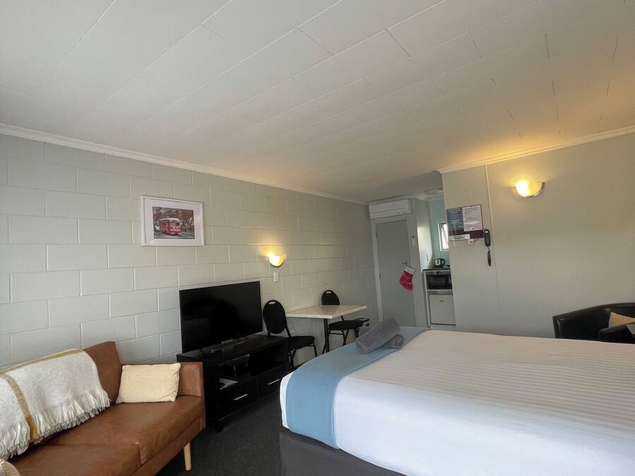 A hotel room with a bed, a sofa, a desk with a chair, a television, and a wall-mounted light fixture.