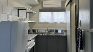 A compact kitchen with a built-in oven, a stainless steel sink, and a window above the countertop. - Kensington Motel (Whangarei)