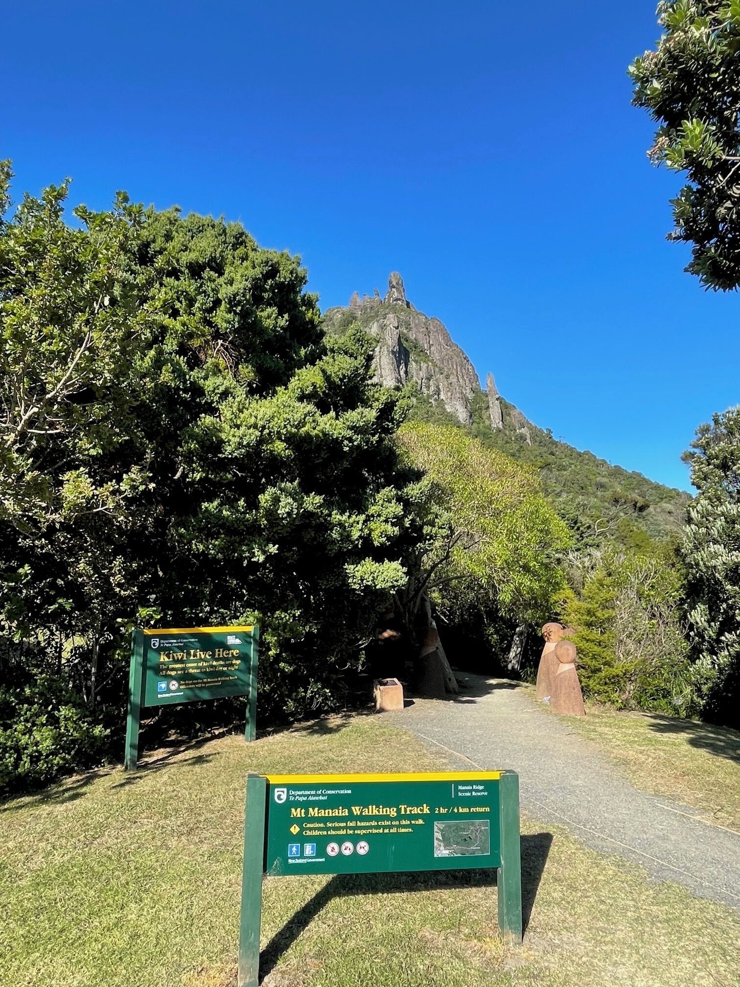A sign for the Mt Manaia Walking Track with a scenic view of a mountain and trees.