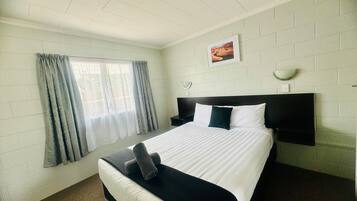 Een hotelkamer met een bed, een raam met gordijnen, een foto aan de muur en een nachtkastje.