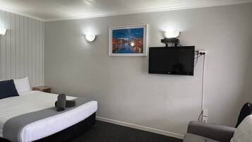 Een hotelkamer met een bed, een grijze bank, een flatscreen televisie aan de muur en een ingelijst schilderij boven de televisie.