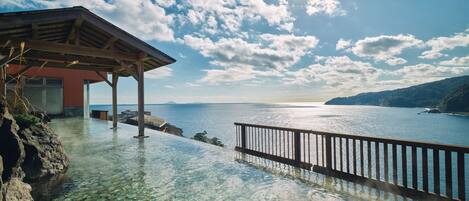 A clear view of a coastal infinity pool with a wooden deck and a metal railing, overlooking the sea.