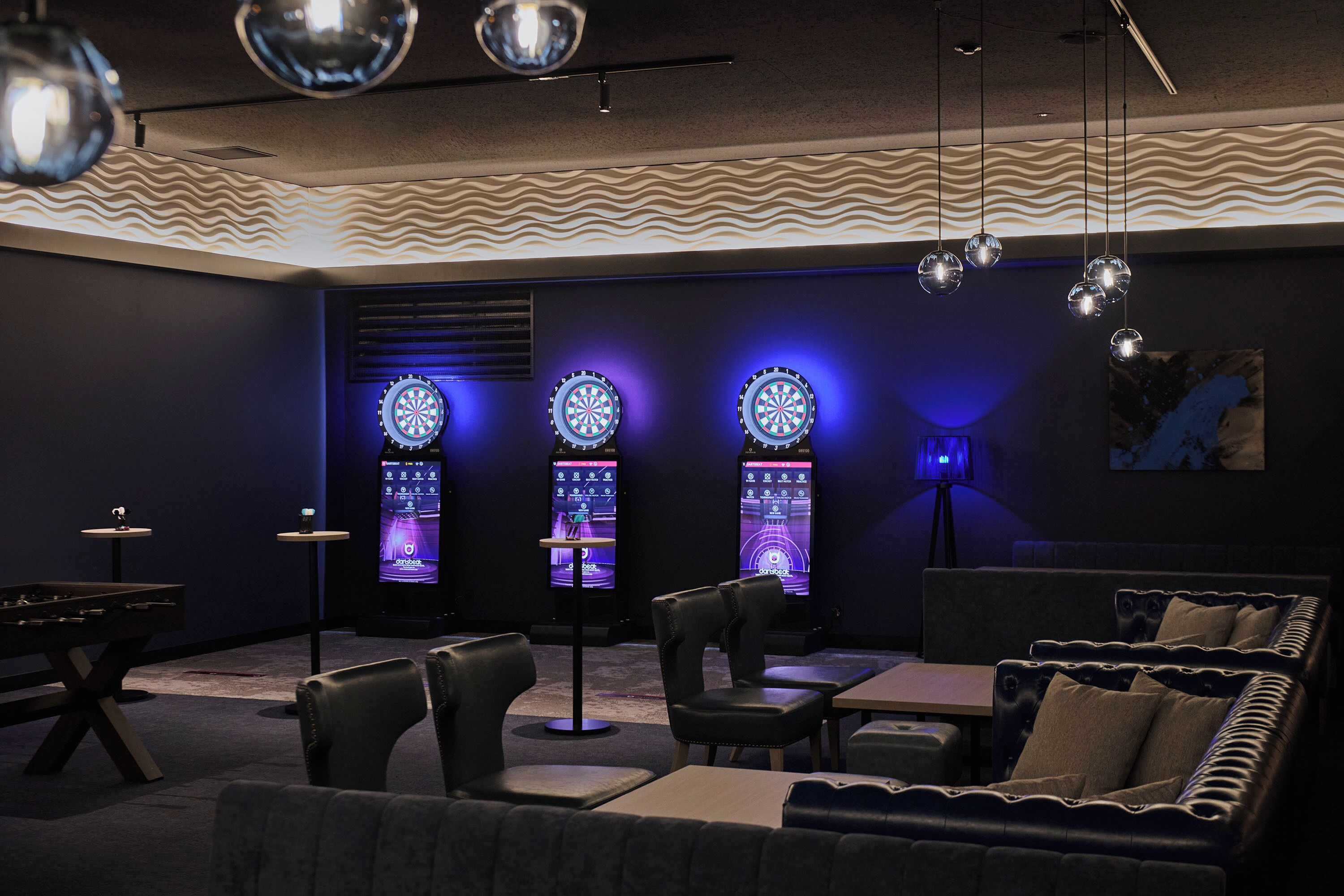 A dimly lit room with a pool table, leather seating, dartboards, and a painting on the wall.