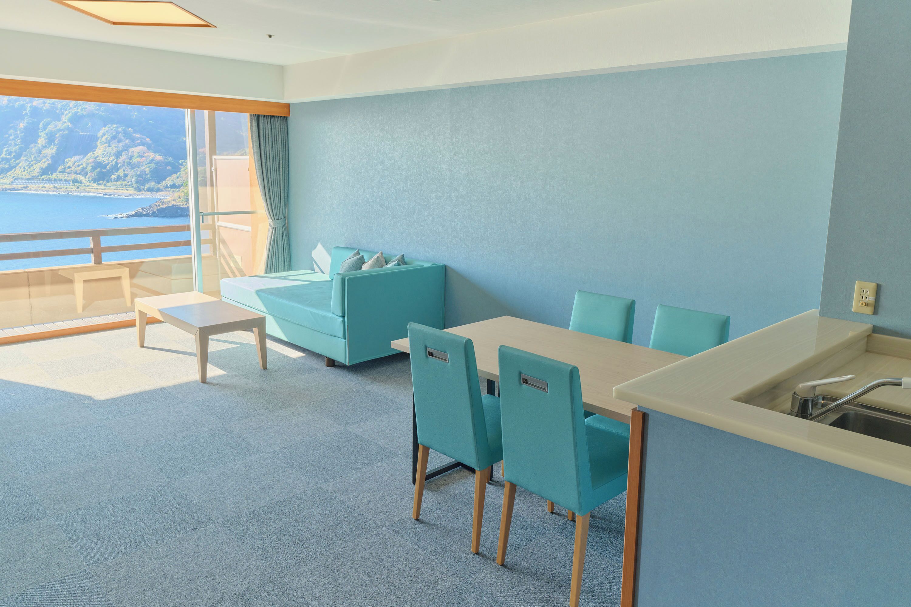 A modern room with a view of the sea, a sofa, chairs, a table, and a sink.