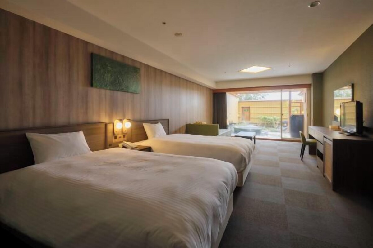A hotel room with two beds, a desk, a chair, a television, and a view of the outdoors.