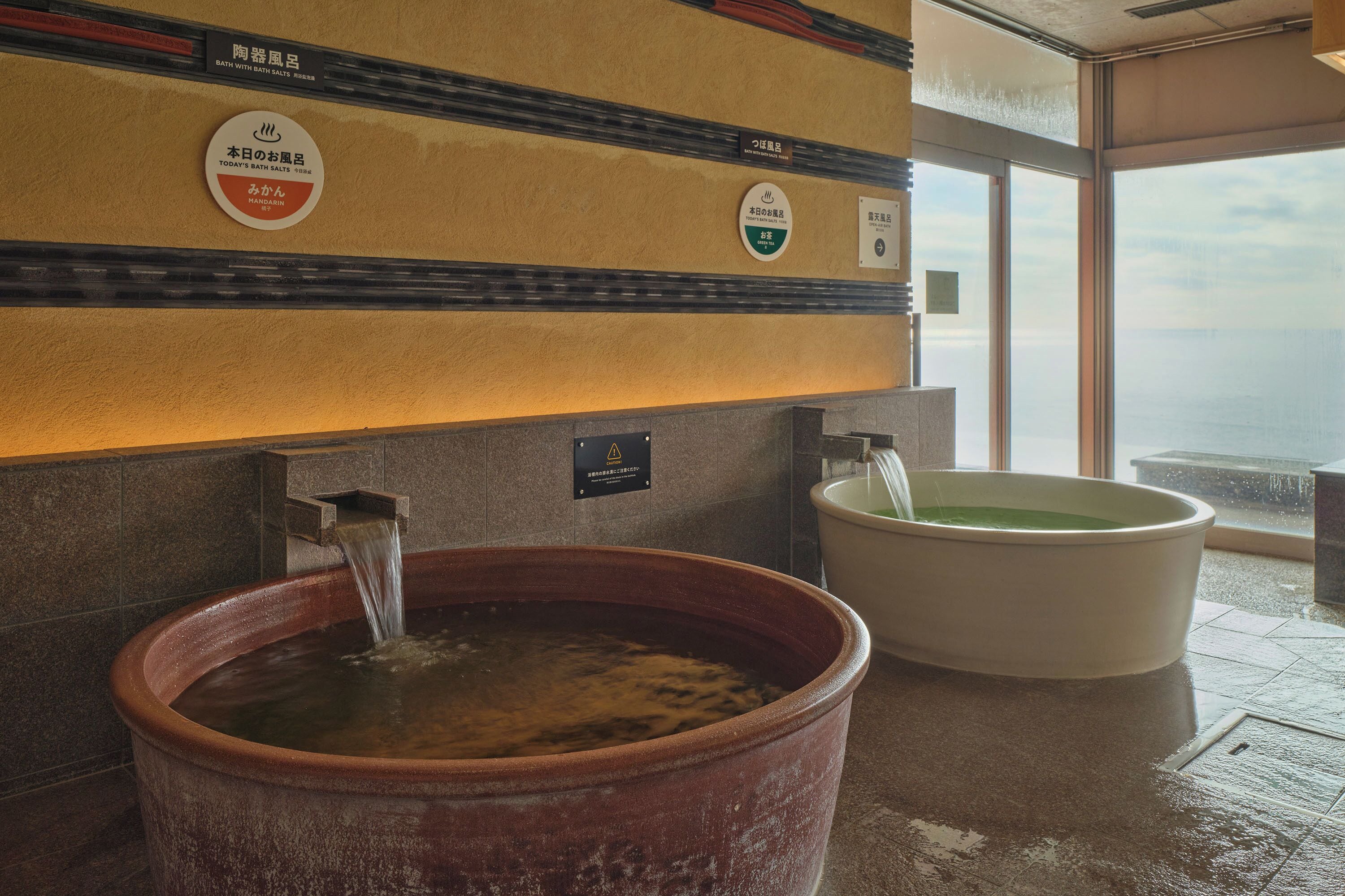 A bath with salt water, a sign indicating it's a bath with salt water, and a view of the sea through large windows.