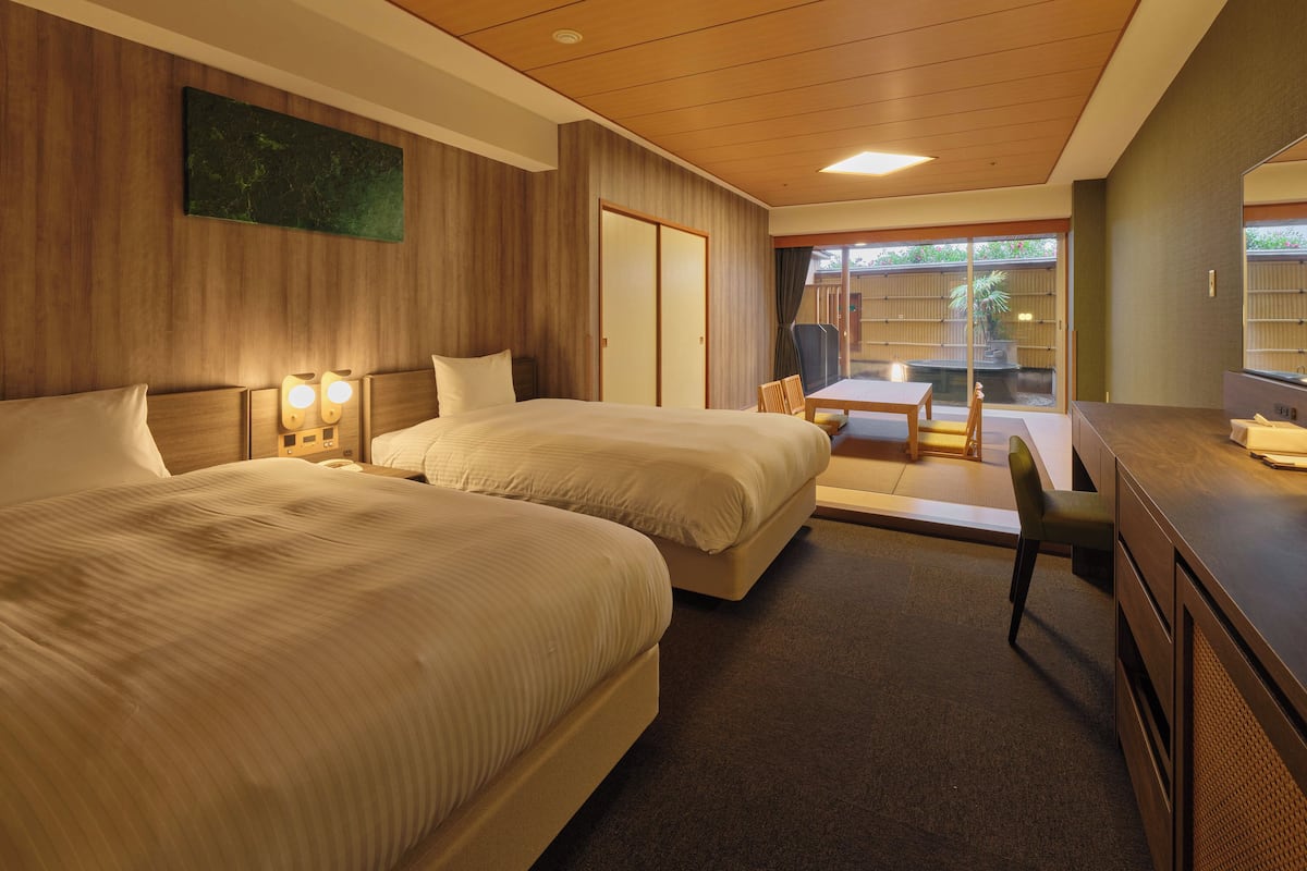 A hotel room with two beds, a desk, and a sliding glass door leading to a patio.