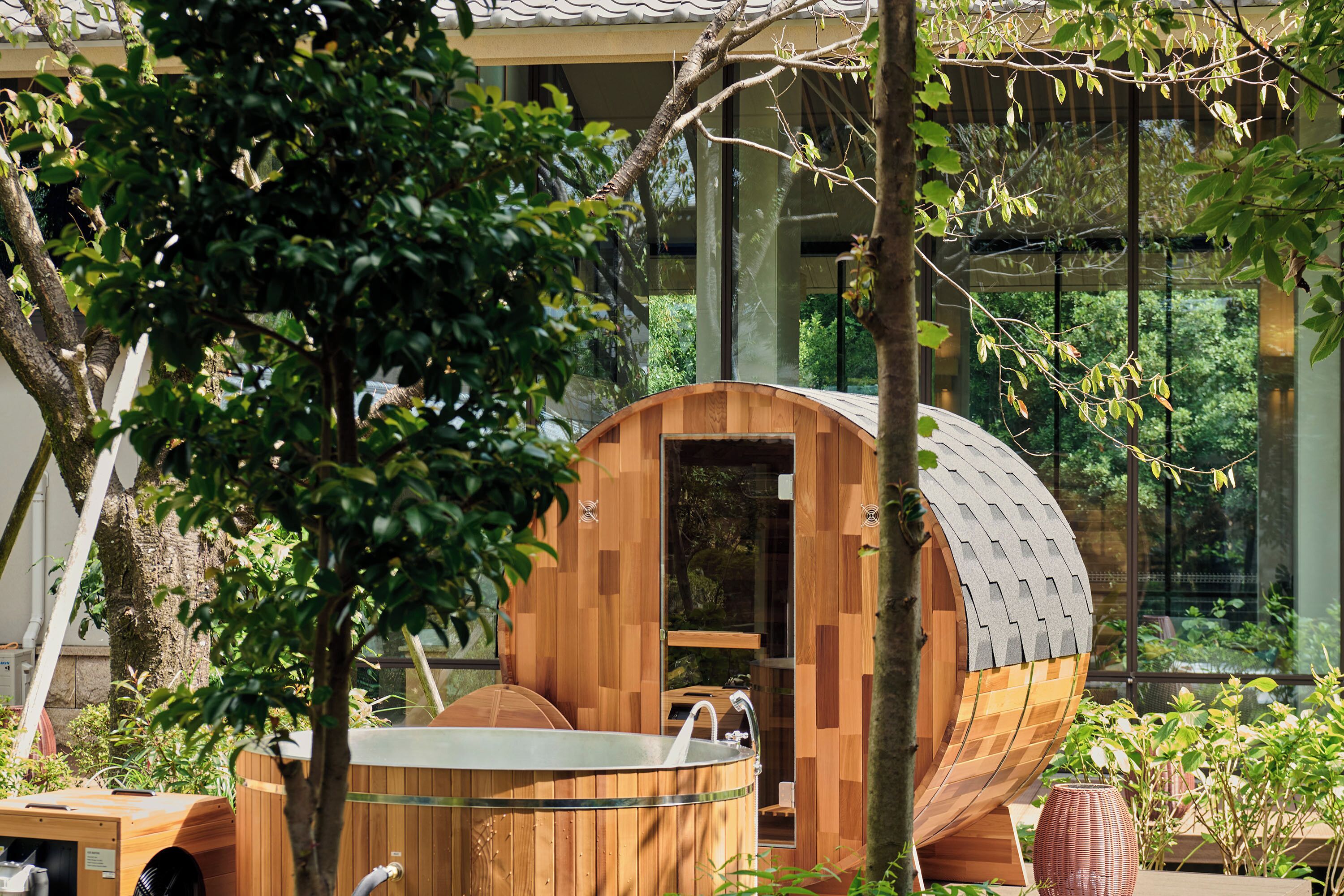 A wooden cylindrical structure with a glass door, a metal sink, and a bench.