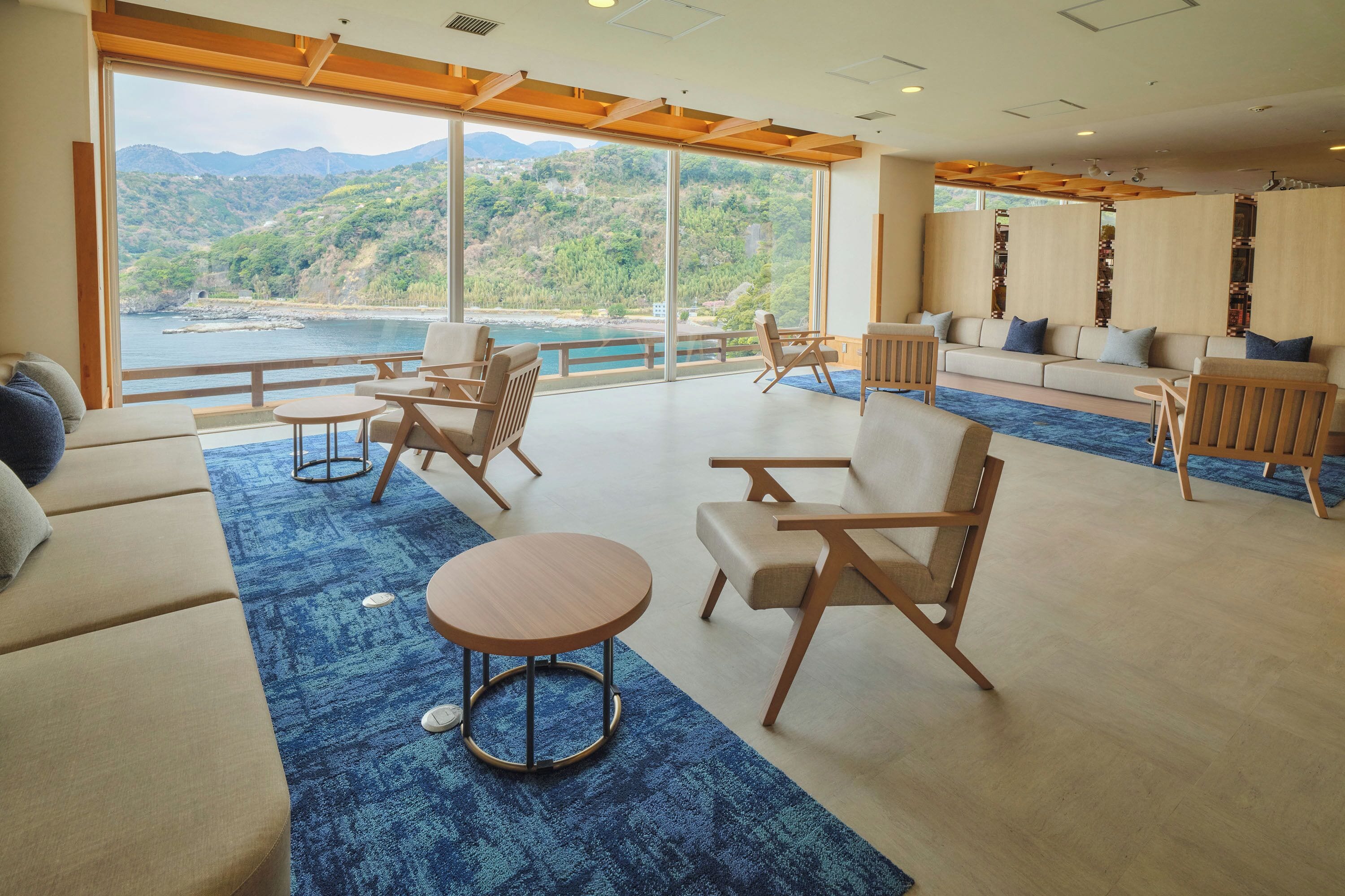 A spacious room with a large window offering a view of a lake and hills, furnished with sofas, chairs, and a small table.