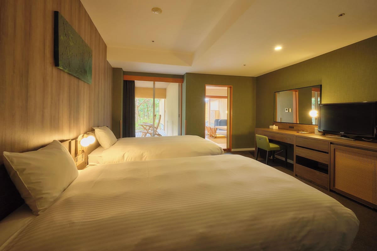 A hotel room with two beds, a desk with a chair, a television, and a large mirror.