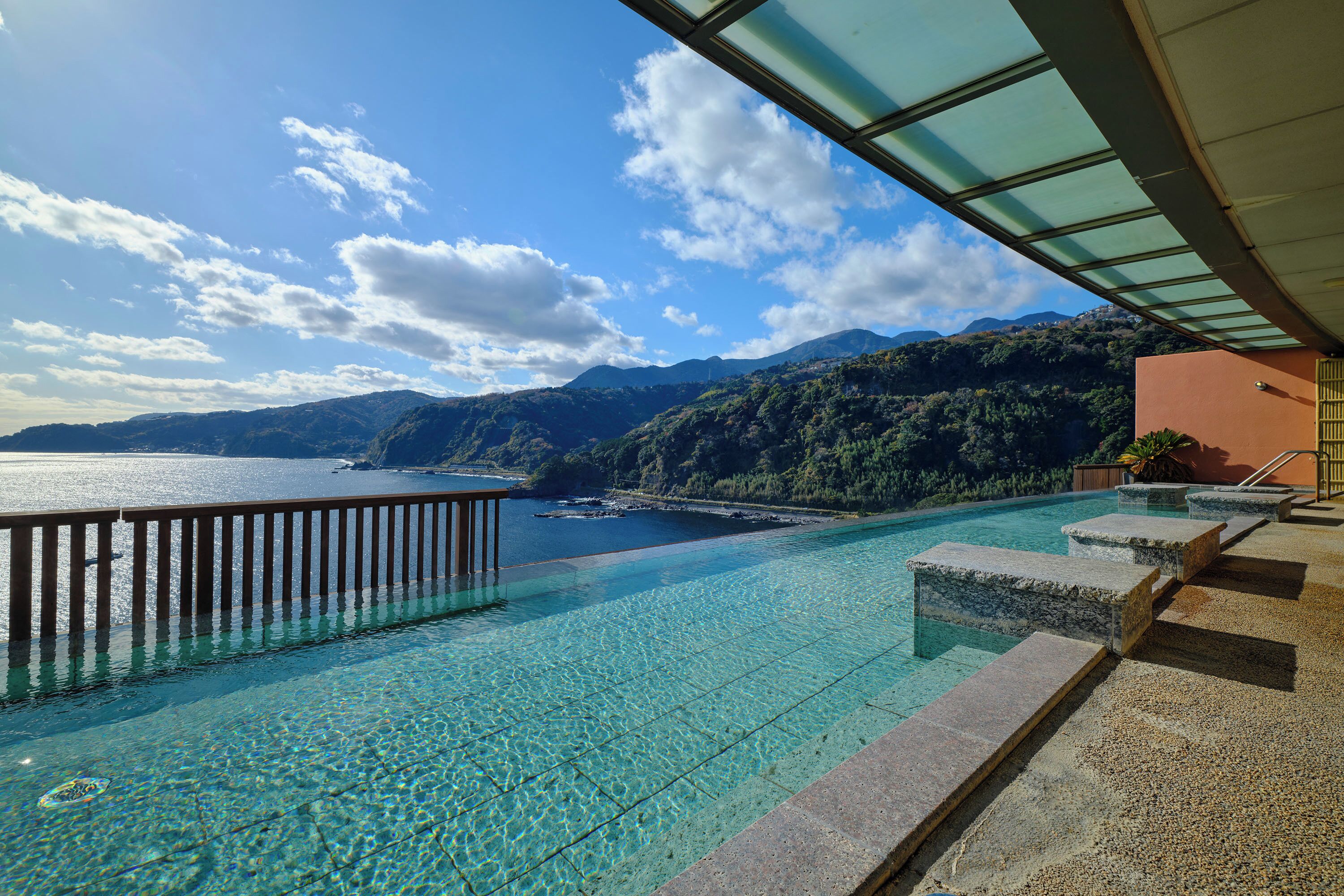 Une piscine d’un bleu éclatant, dotée d’une terrasse en bois et d’escaliers menant à une plateforme surplombant un plan d’eau et des montagnes.
