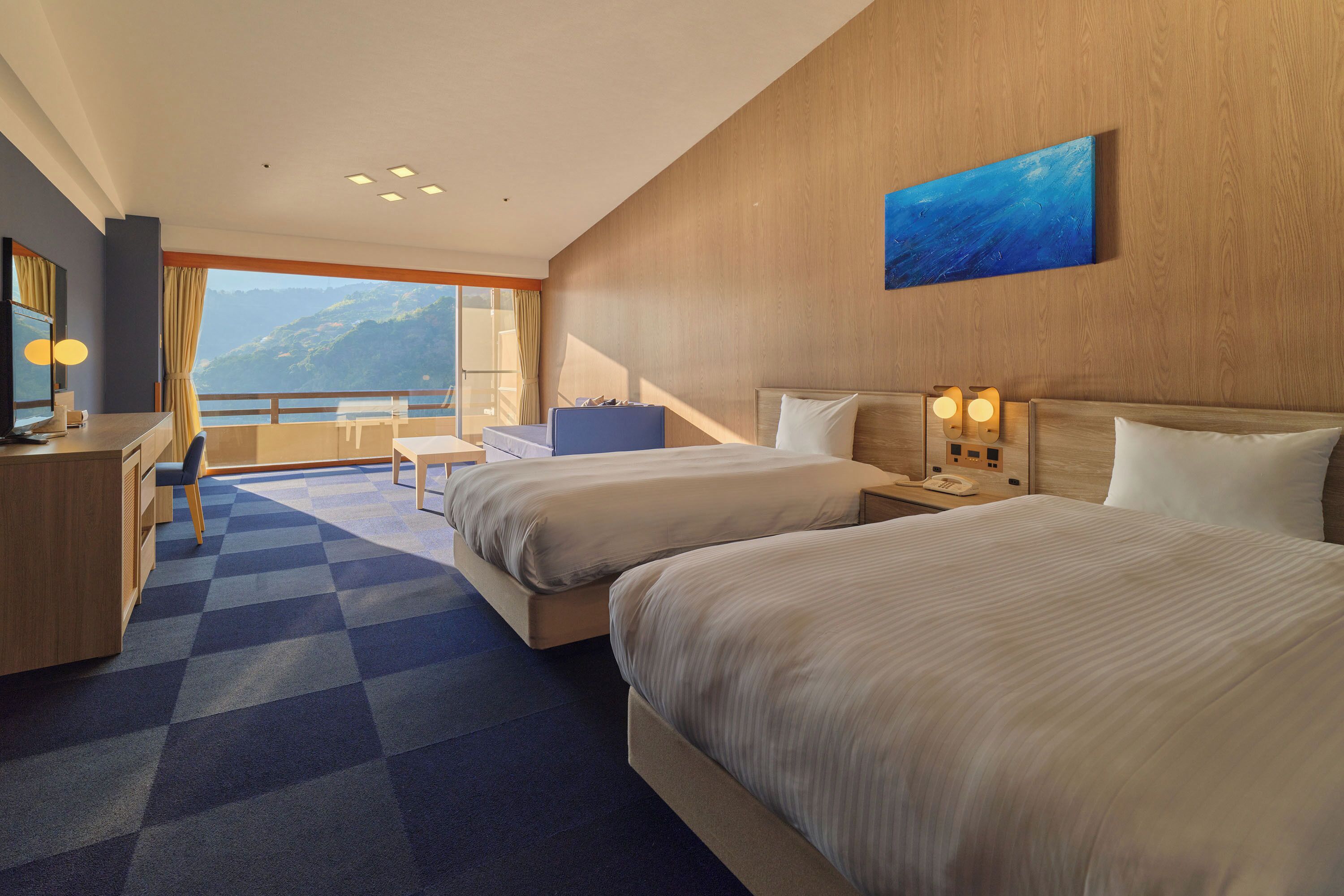 A hotel room with two beds, a desk, a chair, and a view of the mountains.