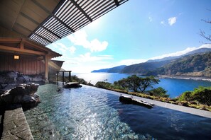 Una vista despejada de una piscina infinita con terraza de madera y vistas al mar y a las montañas.
