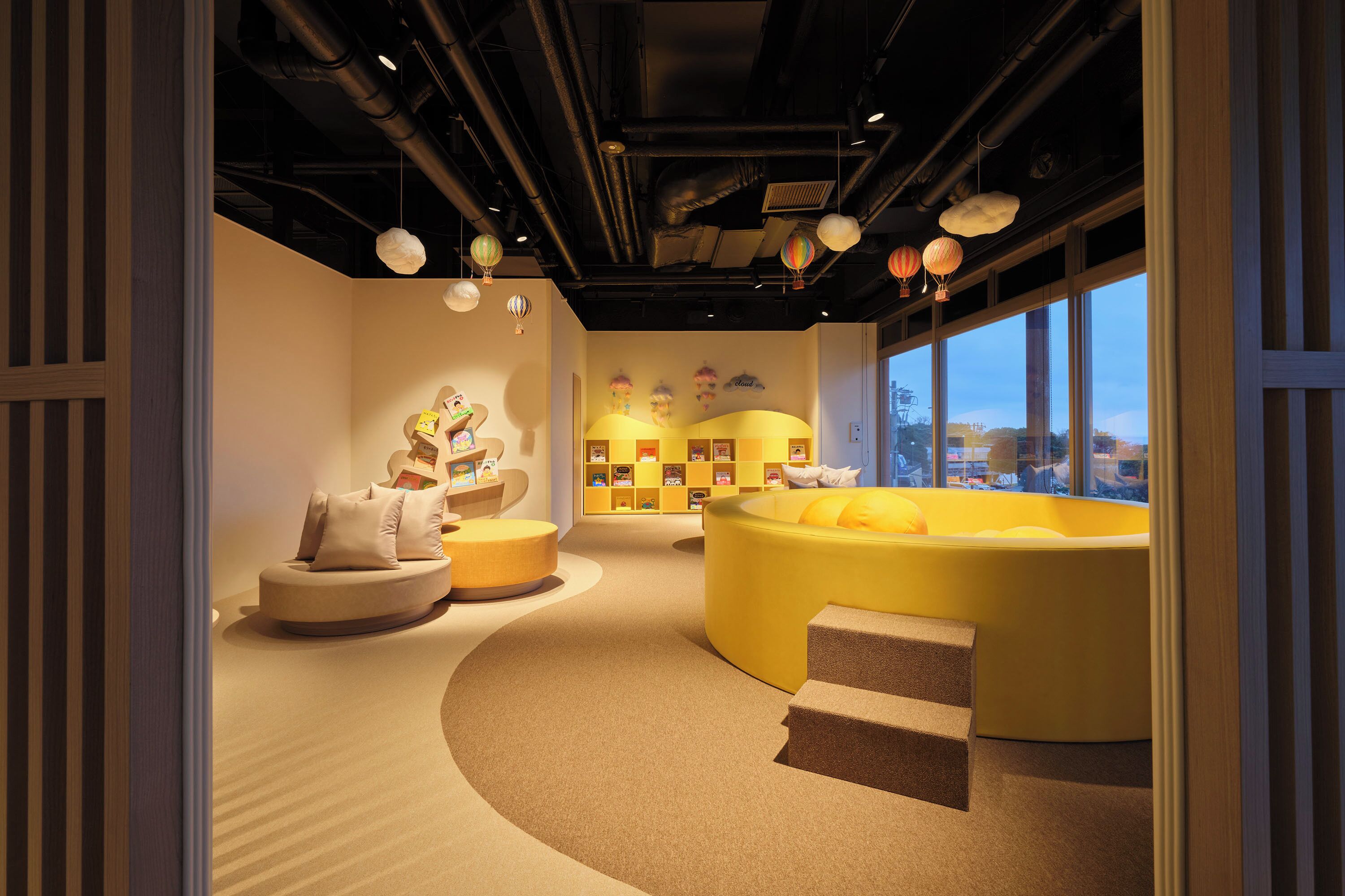 A modern interior with a curved yellow seating area, a white sofa, and a display of books and toys.