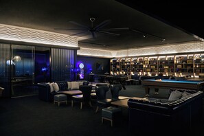 A modern lounge area with a pool table, comfortable seating, and a wall of framed items. - Akazawa Onsen Hotel (Ito)
